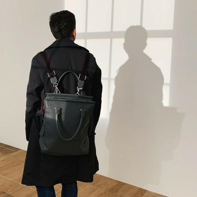 Person with black backpack and dark jacket looking at wall