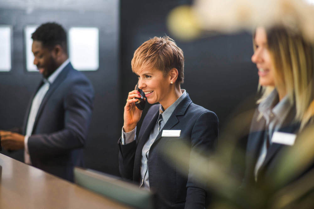 Three receptionists with female employee in the middle on the phone Three receptionists with female employee in the middle on the phone