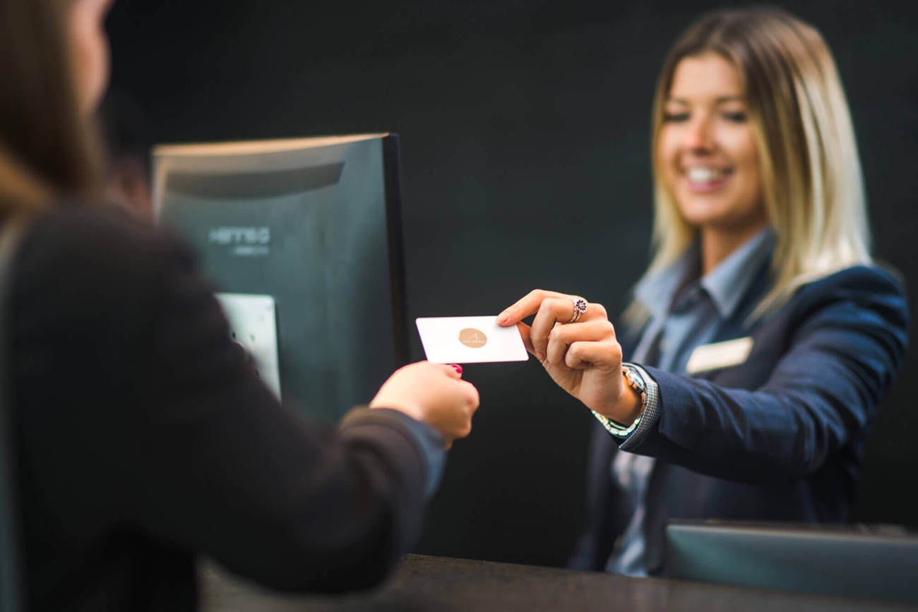 Stay at Apex for our signature warmer welcome Receptionist giving key card to guest at check in